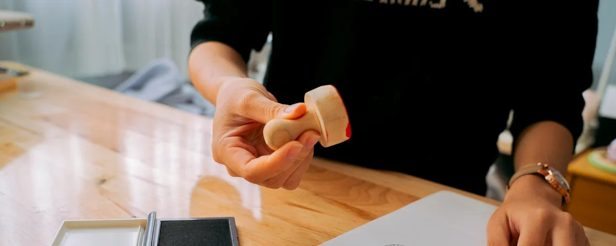 Una mano sellando un documento sobre una mesa de madera
