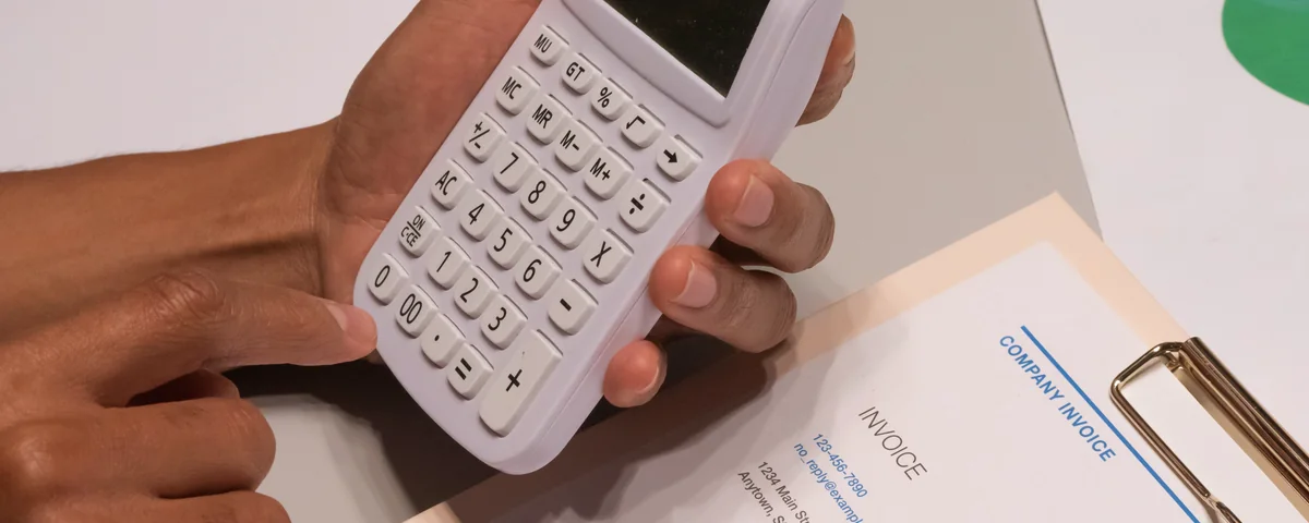 Hände halten einen Taschenrechner neben einer Handelsrechnung auf einem Schreibtisch