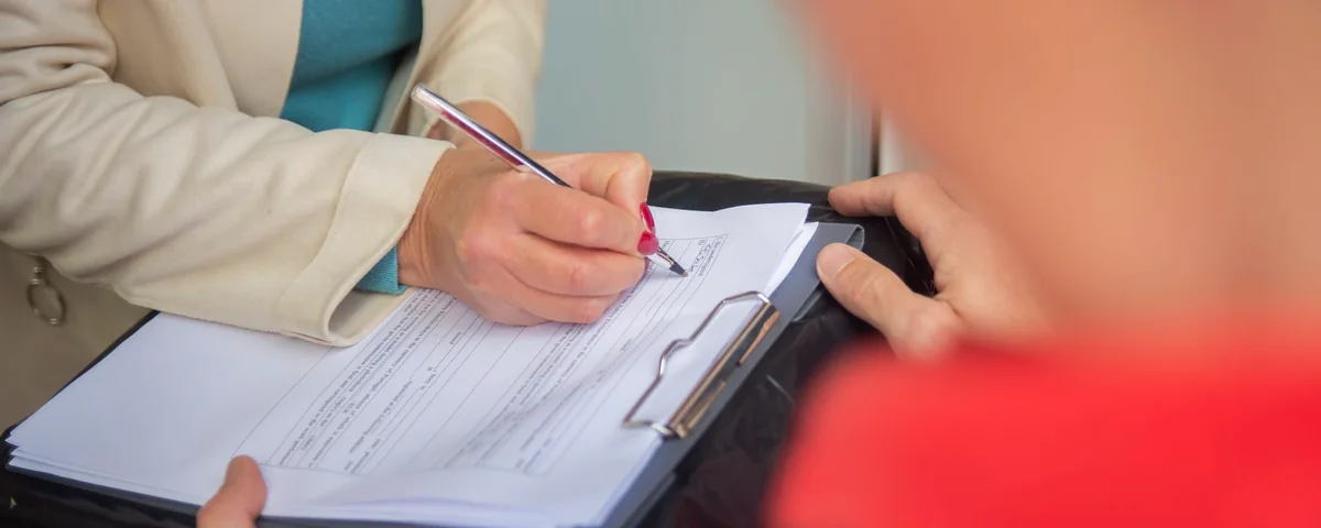 Manos firmando un documento de entrega sobre un portapapeles al recibir un envío de mercancía