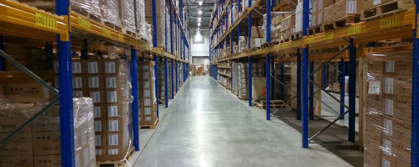 Pasillo de un almacén logístico con estanterías y pallets de cajas preparados para envío
